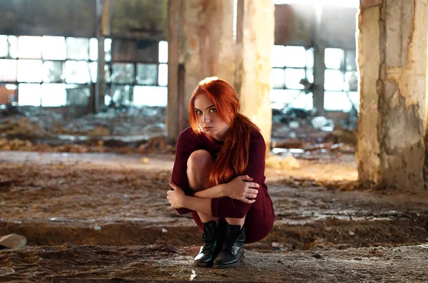 Ragazza dai capelli rossi in una fabbrica abbandonata, seduta sul pavimento, con la paura negli occhi — Foto Stock