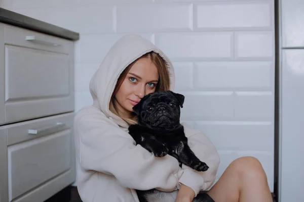 Kız evde kollarında siyah bir köpek tutuyor. — Stok fotoğraf