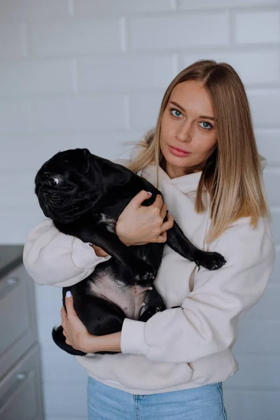 Menina segura um cachorro preto em seus braços em casa — Fotografia de Stock