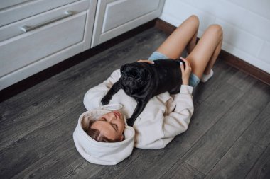 Bir kadın siyah pug köpeğiyle oynuyor.