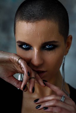 Yüzünde maskara ve ıslak bir yüzle kel bir kız elini yüzüne tutuyor.