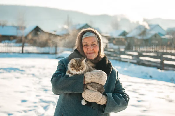 Rus büyükannesinin kollarında bir kedi yavrusu var. Köyü, Sibirya, kış.