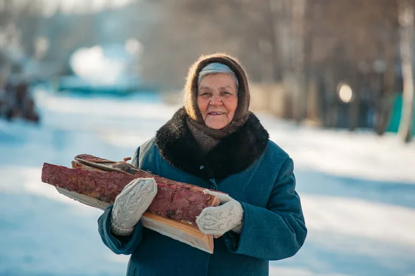 Retrato de una abuela rusa, en el pueblo en invierno, preparando leña, en Siberia —  Fotos de Stock
