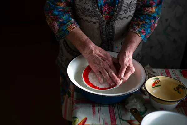 Russian grandmother washes dishes in a basin in the village