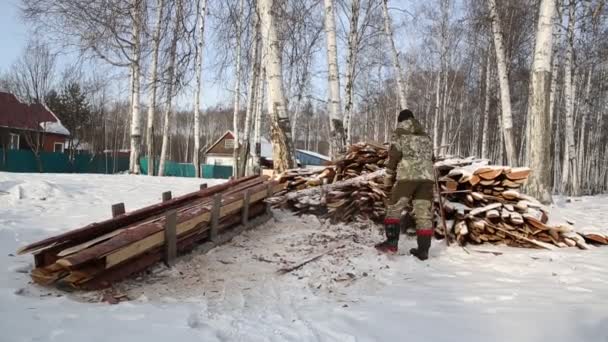Egy favágó fát fűrészel az erdőben télen, Oroszországban tűzifának. — Stock videók