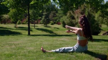 İnce kadın sicimin üzerinde çimlerin üzerinde oturarak esneme egzersizi yapıyor.