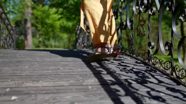 Primer plano de una mujer con los pies en sandalias caminando sobre una cubierta de madera en un día soleado — Vídeos de Stock