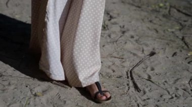 Güneşli bir günde kumsalda yürüyen, ayakları sandaletli bir kadının yakın çekimi.