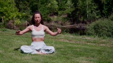 Asyalı kadın parkta lotus pozisyonunda meditasyon yapıyor.