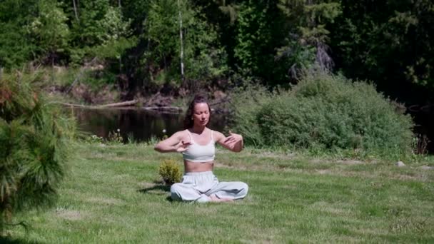 Namaste asana jogi praktyki kobieta wykonuje ćwiczenia oddechowe i medytuje podczas jogi w parku w przyrodzie, siedzi na zielonej trawie — Wideo stockowe