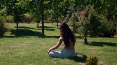 Kadın, güneşli bir yaz gününde öğleden sonra çimlerin üzerinde oturarak nefes egzersizleri ve esneme egzersizleri yapıyor.