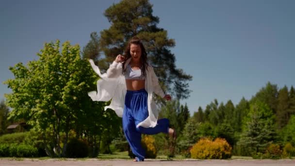 Азиатка танцует латиноамериканский танец в парке. Женщина, занимающаяся наружными движениями — стоковое видео