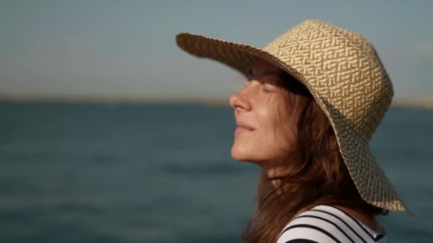 Портрет жінки середнього віку на прогулянці уздовж моря з великим капелюхом на її голові — стокове відео
