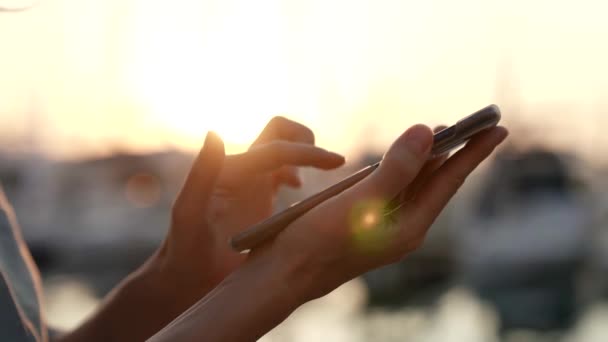 Nahaufnahme mit den Strahlen der untergehenden Sonne, eine Frau, die ein Smartphone in der Hand hält, ist ein modernes Konzept eines Anwenders drahtloser Technologie. — Stockvideo