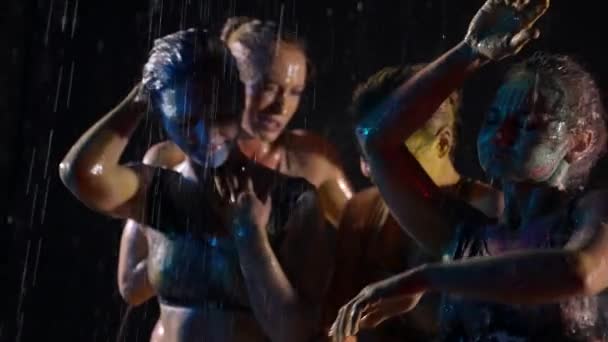 Performance de arte cuatro mujeres bailando con pintura en la piel bajo la lluvia sobre un fondo negro — Vídeo de stock