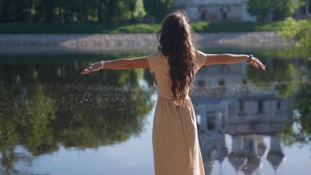 긴 머리를 가진 날씬 한 여자가 호숫가에서 새로운 날을 맞아 하늘을 향해 손을 들고 — 비디오