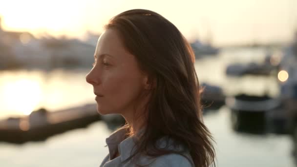 Portré egy titokzatos nőről, aki élvezi a naplementét a kikötőben. Boldognak látszol, szabadnak érzed magad a nyaraláson. — Stock videók