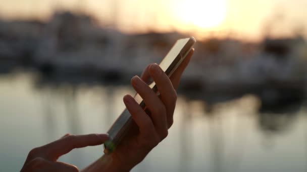 Крупным планом женские руки с помощью мобильного телефона на улице под заходящим солнцем — стоковое видео