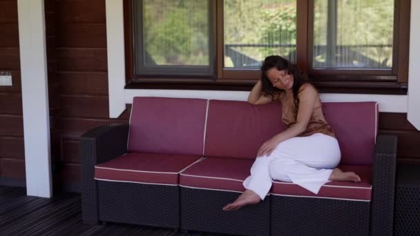 Счастливая женщина отдыхает на веранде загородного дома — стоковое видео