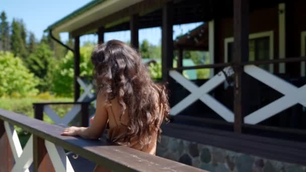 Uma mulher misteriosa feliz está de pé na varanda da casa pela manhã apreciando o sol. Estou a caminhar no parque. férias no país. — Vídeo de Stock