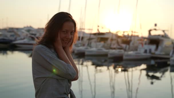 Portrait d'une femme au soleil couchant profitant d'une promenade au bord de la mer dans le port avec des yachts. Vacances en plein air en plein air. Le concept d'un mode de vie sain et heureux. — Video