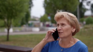 Şehrin caddesinde cep telefonuyla konuşan yaşlı bir kadının yakın çekimi. Yaşlı bir kadın emekli açık havada bir cep telefonuyla konuşuyor. Bir telefon..