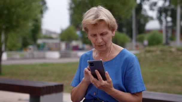 Een oudere vrouw met een mobiele telefoon schrijft een sms tijdens een wandeling in het park — Stockvideo