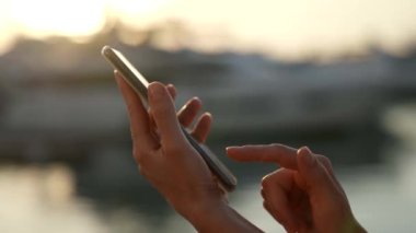 Bir cep telefonu kullanarak, güneşin batışında nazik kadın parmaklarının ışınlarıyla mesaj gönderme.