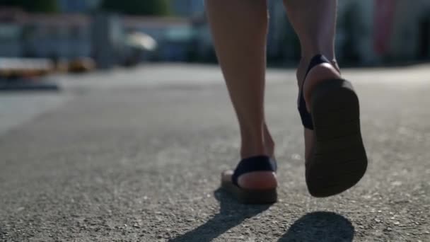 Primer plano de una mujer caminando por un camino de asfalto al atardecer — Vídeos de Stock