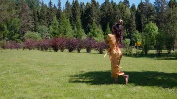 Eine Hippie-Frau dreht sich in einem grünen Park und genießt die Einheit mit der Natur, um in den Sonnenstrahlen zu baden — Stockvideo