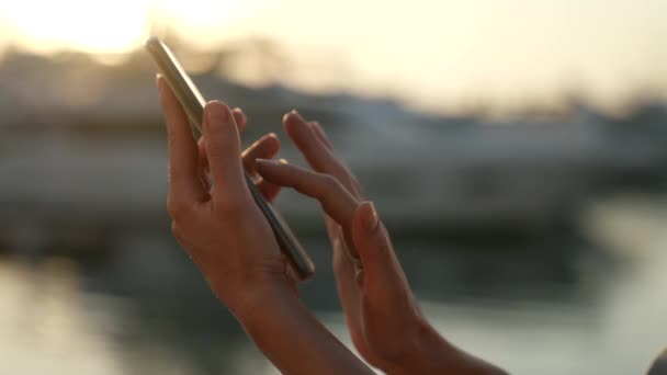 Крупным планом женщины, держащей телефон руками и бегущей пальцами по сенсорному экрану на улице вечером — стоковое видео