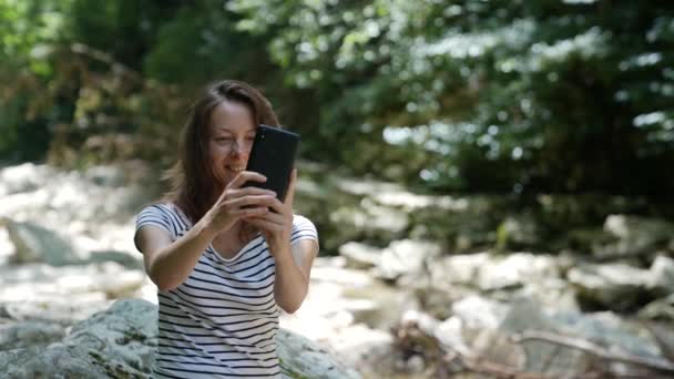 Câmera lenta uma mulher de férias senta-se nas montanhas e tira uma foto de si mesma em seu telefone — Vídeo de Stock