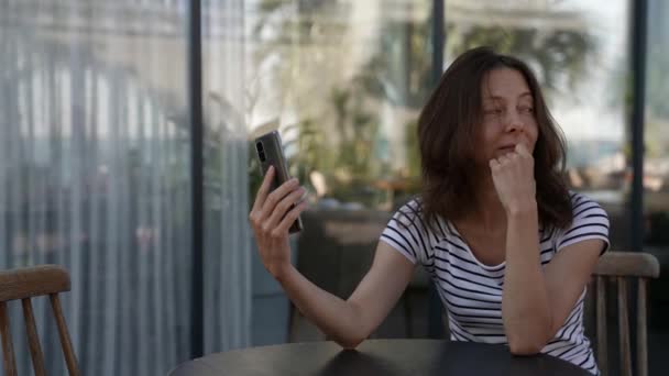 Элегантная взрослая женщина сидит на веранде в ресторане и разговаривает по видеосвязи на телефоне — стоковое видео