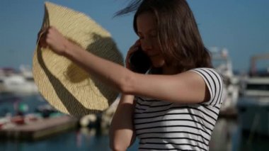 Ağır çekimde orta yaşlı güzel bir kadın kafasından büyük bir şapka çıkarır ve yürürken telefonla konuşur.