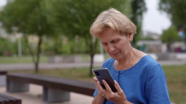 Женщина в отставке использует мобильный телефон на улице, чтобы общаться со своей семьей — стоковое видео