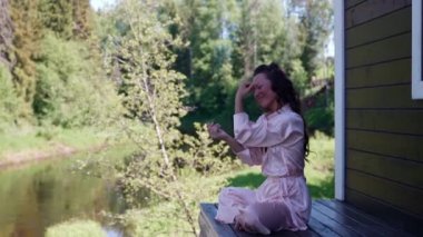 Yüzünde gülümseme olan mutlu bir kadın lotus pozisyonunda oturarak doğada nefes egzersizleri yapıyor.