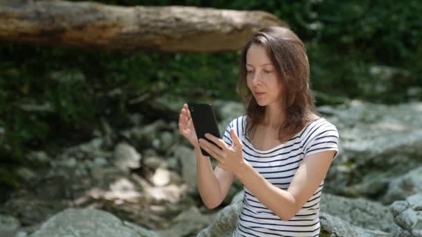 Uma mulher adulta elegante na natureza nas montanhas usa seu telefone para ver a rota na navegação para uma caminhada — Vídeo de Stock