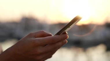 Gün batımında ya da gün doğumunda kumsalda akıllı telefon kullanan bir kadının yan görüntüsü. Genç kadınların ellerine yakın çekim