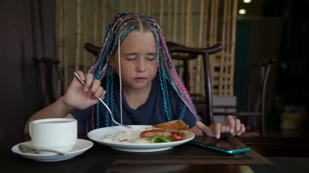 Красивый подросток наслаждается едой в ресторане и листает через социальную сеть на своем телефоне — стоковое видео