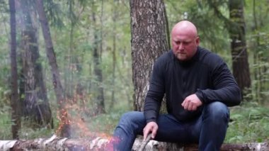 Bir adam ateşin yanında oturmuş düşünceli bir yüzle alevli ateşe bakıyor. Bir erkek gezgin, turizm kavramı olan vahşi yaşamla çevrili bir kamp ateşinin yanında dinlenir.