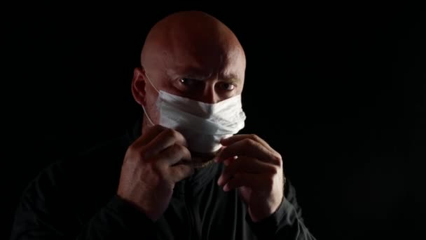Porträtt av en vuxen skallig man i medicinsk mask i ansiktet. Isolerad på en svart bakgrund. Begreppet pandemi, skydd och hälsa. — Stockvideo