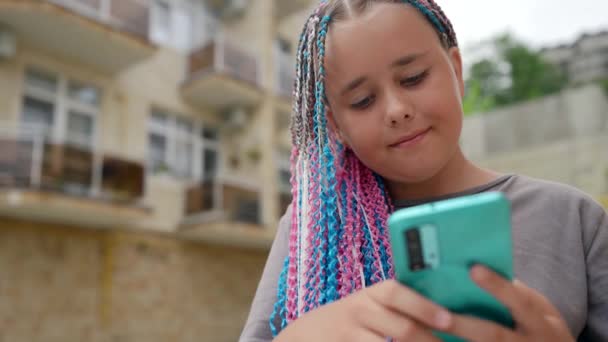 Piękna nastolatka dziewczyna wykorzystuje telefon komórkowy do komunikacji wideo na głowie dziecka afro-warkocze — Wideo stockowe