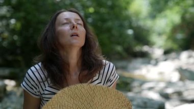 Gülümseyen neşeli doğal bir kadının portresi. Doğada oturuyor ve sıcaktan büyük bir şapka sallıyor.