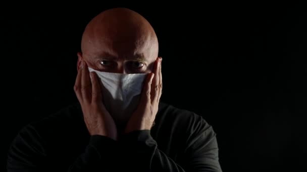 Kale volwassen noodlijdende man met een medisch masker op een zwarte geïsoleerde achtergrond — Stockvideo