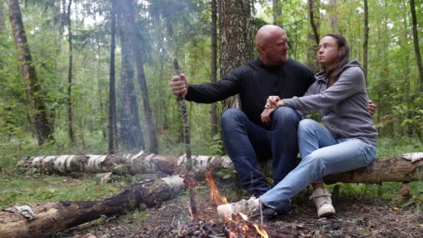 Um casal bonito e uma família estão sentados na floresta enquanto viajam perto de uma fogueira se aquecendo — Vídeo de Stock