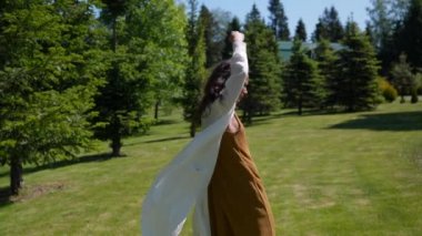 İnce kız doğada uzun beyaz bir tunikle dans ediyor.