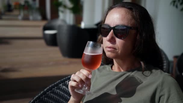 Eine erfolgreiche Frau mittleren Alters entspannt sich in einer Bar auf der Veranda, trinkt ein Glas kalten rosa Champagner und genießt das Leben — Stockvideo