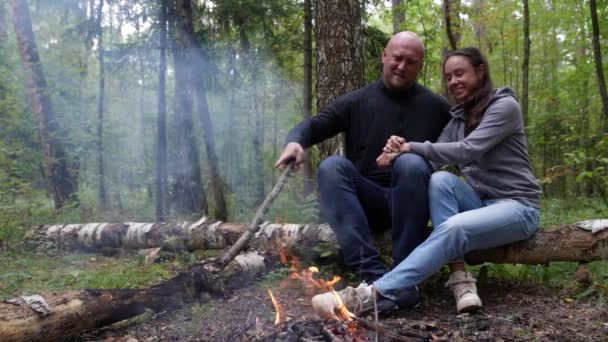 Un cuplu căsătorit într-o excursie prin pădure s-a oprit să se încălzească lângă foc și să-și amintească cazuri amuzante în conversație. — Videoclip de stoc