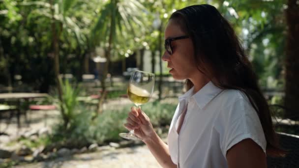 An adult woman a wine connoisseur is relaxing in a bar on the street with a glass of cold white wine during the day at the resort — Stock Video