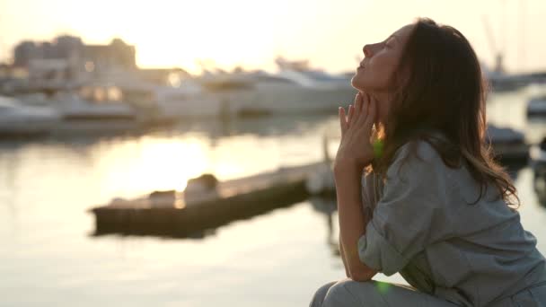 Uma turista bem sucedida senta-se na praia com um iate estacionado e medita ao pôr do sol — Vídeo de Stock